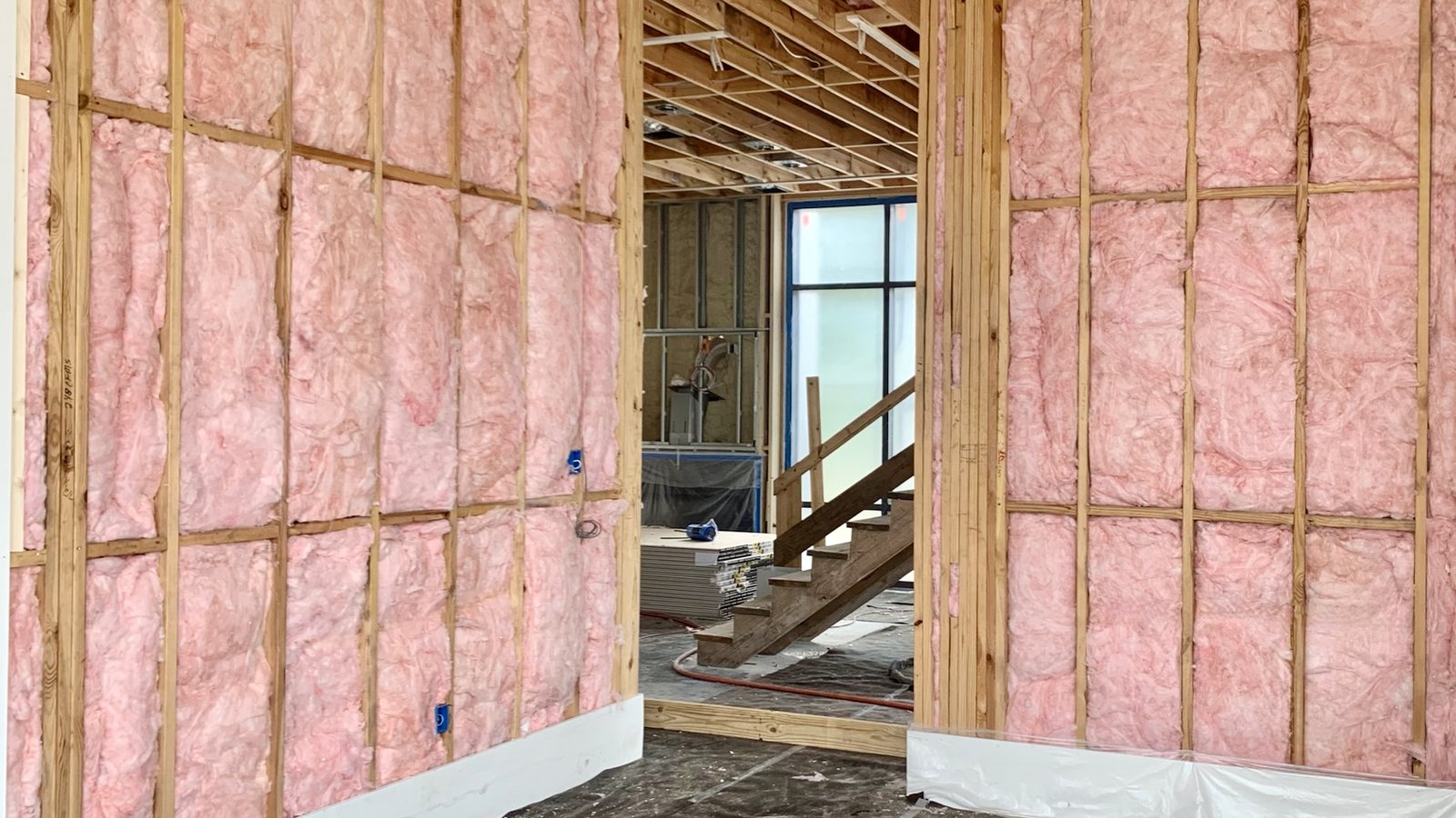 Two new-construction wood-frame walls with unfaced fiberglass batts filling every stud bay, cut to fit between rows of horizontal blocking, seen through a doorway.