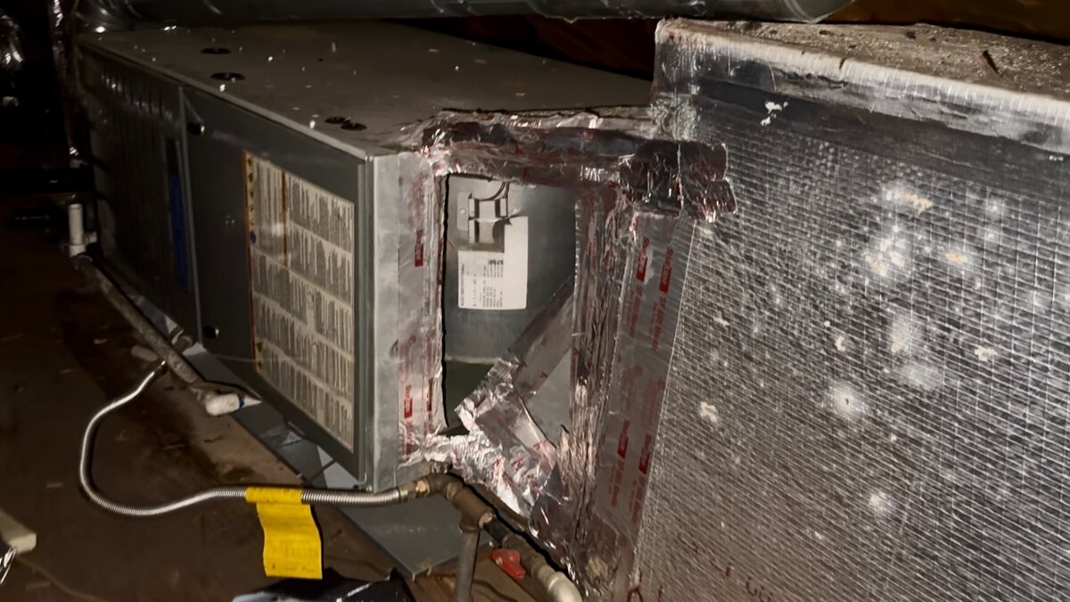 A ductboard return box at an attic air handler that has collapsed away from the cabinet, leaving a wide gap along the seam with torn foil tape hanging loose.