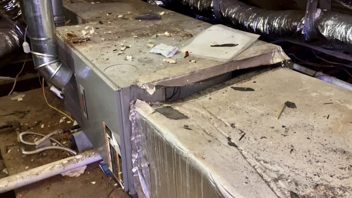 A return plenum separated from the top seam of an attic air handler, with construction debris and insulation scraps scattered across the ductboard.