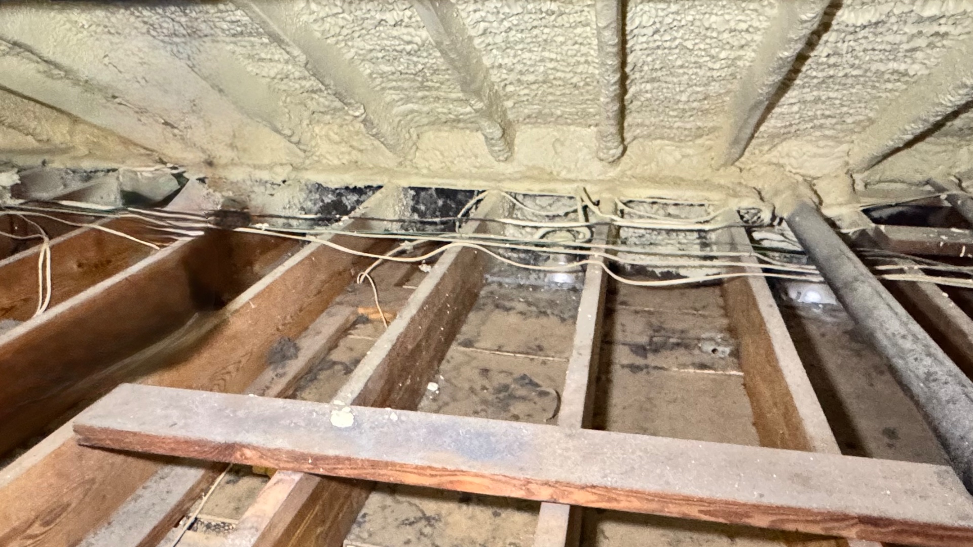 Roofline spray foam stopping short of the exterior-wall perimeter, exposing framing and remaining cellulose.